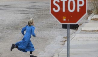 In this Dec. 16, 2014, photo, a girl runs past a street sign in Hildale, Utah. The sister cities of Hildale and Colorado City, Ariz., once run by polygamist leader Warren Jeffs, are split between loyalists who still believe he is a victim of religious persecution and defectors who are embracing government efforts to pull the town into modern society. (AP Photo/Rick Bowmer)