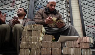 FILE - In this Monday, Jan. 12, 2015 file photo, An Afghan money changer, right, counts a pile of currency at the Money and Exchange Market in Kabul. Afghanistan’s fragile economy has lost around a third of its value in the past year as the international military and aid organizations that poured in cash for more than a decade have drastically scaled back after U.S. President Barack Obama declared an end to the 13-year war against the Taliban _ leaving the government struggling for funds and key sectors lacking investment, economists, analysts and officials said. (AP Photo/Massoud Hossaini, FIle)