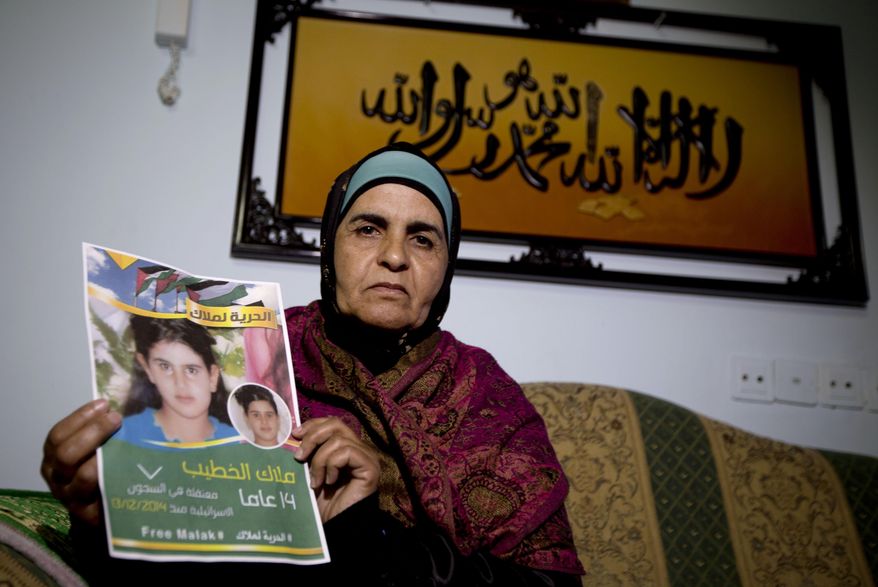 In this Tuesday, Jan. 27, 2015 photo, Palestinian Khawla Al-Khatib, holds a poster of her 14-year-old daughter Malak al-Khatib, detained in Israel, in the village of Beitin near the West Bank city of Ramallah. The Palestinian suspect, charged with stone throwing and possession of a knife, entered the courtroom and was sentenced to two months in prison. The scene has played out like many others in Israeli military courts. Except this time, the suspect was a 14-year-old girl. Malak al-Khatib was arrested last month near her sleepy village in the West Bank. Hers is a rare case of a female Palestinian minor held by Israel that has gripped Palestinians, who say her treatment demonstrates Israel’s excessive measures against stone-throwing youth. (AP Photo/Majdi Mohammed)
