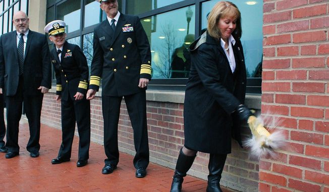 Vice Adm. Willy Hilarides (center) watches his wife Beverly break a bottle against the wall during the reopening ceremony for the Naval Sea Systems Command&#x27;s headquarters building at the Washington Navy Yard. On the far left is Rear Admiral Katherine L. Gregory. The building was the site of the shooting rampage on Sept. 16, 2013. (U.S. Navy)