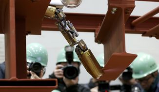 In this Thursday, Feb. 5, 2015 photo, photographers take photos of a remote-controlled robot that looks like an enlarged fiberscope crawling down into the mock-up of a primary containment chamber during a demonstration for the media at a government facility in Hitachi, Ibaraki Prefecture, northeast of Tokyo. The snake-like robot, developed by Japanese electronics giant Hitachi and its nuclear affiliate Hitachi-GE Nuclear Energy, is ready to examine in April the damage inside Unit 1 reactor at the Fukushima dai-ichi nuclear plant, wrecked by the march 2011 earthquake and tsunami. (AP Photo/Shizuo Kambayashi)