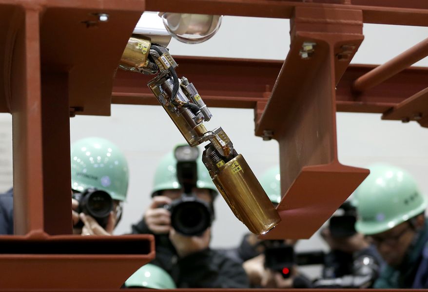 In this Thursday, Feb. 5, 2015 photo, photographers take photos of a remote-controlled robot that looks like an enlarged fiberscope crawling down into the mock-up of a primary containment chamber during a demonstration for the media at a government facility in Hitachi, Ibaraki Prefecture, northeast of Tokyo. The snake-like robot, developed by Japanese electronics giant Hitachi and its nuclear affiliate Hitachi-GE Nuclear Energy, is ready to examine in April the damage inside Unit 1 reactor at the Fukushima dai-ichi nuclear plant, wrecked by the march 2011 earthquake and tsunami. (AP Photo/Shizuo Kambayashi)