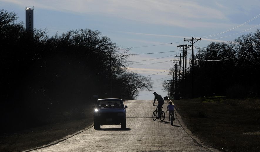 ADVANCE FOR USE SUNDAY, FEB. 15 - In this photo taken Jan. 28, 2015, Brad Harvell watches a car pass and checks on his 7 year-old daughter Lucretia as they ride bicycles along E. 16th Street in Cisco, Texas. The brick road is one of the remains of the Bankhead Highway, the second transcontinental highway across the United States, a third of which passed through Texas and was known as "The Broadway of America." (AP Photo/The Abilene Reporter-News, Ronald W. Erdrich) MANDATORY CREDIT