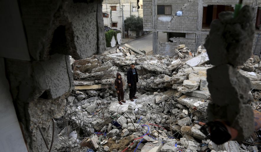 In this Wednesday, Nov. 26, 2014 photo, Mohammed Al-Bayoumi, 39, and his son Mahmoud stand on the rubble of their family home in the Nusseirat refugee camp in the central Gaza Strip. A July 31 Israeli airstrike killed 13 people from two families, including his son. The number of civilian deaths has been a key issue in the highly charged battle over the dominant narrative of last summer’s 50-day war, the third and most destructive confrontation between Israel and Hamas since 2008. (AP Photo/Adel Hana)