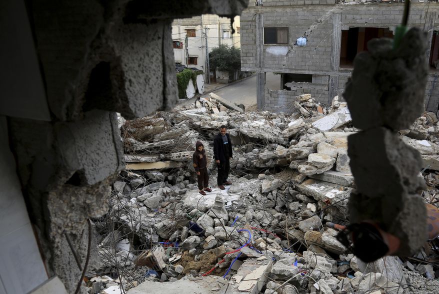 In this Wednesday, Nov. 26, 2014 photo, Mohammed Al-Bayoumi, 39, and his son Mahmoud stand on the rubble of their family home in the Nusseirat refugee camp in the central Gaza Strip. A July 31 Israeli airstrike killed 13 people from two families, including his son. The number of civilian deaths has been a key issue in the highly charged battle over the dominant narrative of last summer’s 50-day war, the third and most destructive confrontation between Israel and Hamas since 2008. (AP Photo/Adel Hana)