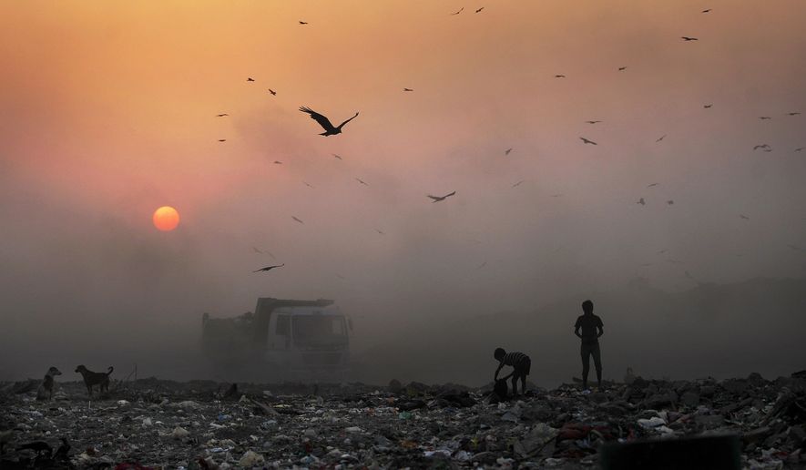 A blanket of smoke filters the setting sun as young ragpickers search for reusable material at a garbage dump in New Delhi. India and a host of other countries are demanding payments as part of the Paris Agreement to reduce their levels of pollution. (Associated Press/File)