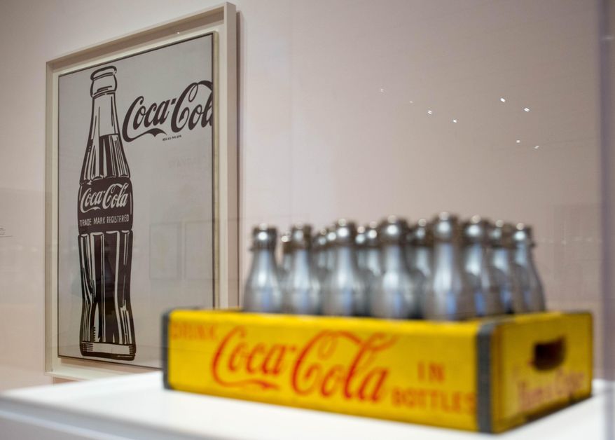 A piece by artist Andy Warhol, left, is displayed next to a case of Coca-Cola bottles at the High Museum's new exhibit, "The Coca-Cola Bottle: An American Icon at 100", Wednesday, Feb. 25, 2015, in Atlanta. The exhibit, opening Feb. 28, explores the iconic design and creative legacy of the familiar soda bottle as art. (AP Photo/Branden Camp)