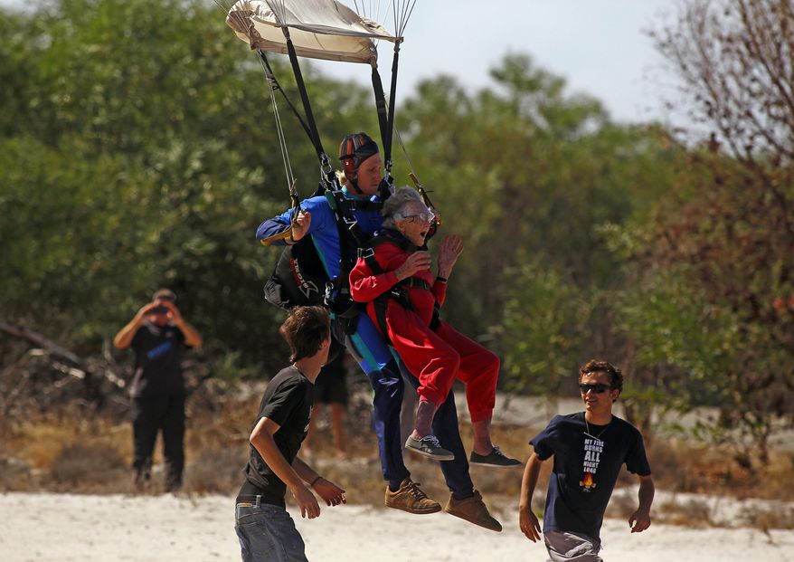 Centenarian Georgina Harwood, center right, gestures as she lands with Jason Baker, center left, after her tandem parachute jump forming part of her birthday celebrations, in Cape Town, South Africa, Saturday, March 14, 2015. Harwood, who celebrated her 100th birthday on Tuesday, completed her third tandem parachute jump in front of family and friends. (AP Photo/Schalk van Zuydam)
