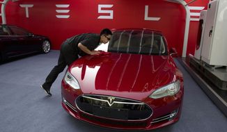 FILE - In this April 22, 2014 file photo, a worker cleans a Tesla Model S sedan before a event to deliver the first set of cars to customers in Beijing. Tesla Motors on Thursday, March 19, 2015 said it is updating its Model S electric car to help ease drivers&#39; worries about running out of battery charge.  (AP Photo/Ng Han Guan, File) **FILE**