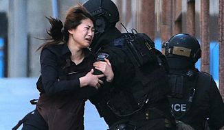 FILE - In this Dec. 15, 2014 file photo, a hostage runs to armed tactical response police officers for safety after she escaped from a cafe under siege at Martin Place in the central business district of Sydney, Australia.  For a country of just 24 million that is thousands of miles from Syria and Iraq, Australia has been unusually fertile ground for Islamic State recruiters. (AP Photo/Rob Griffith, File)