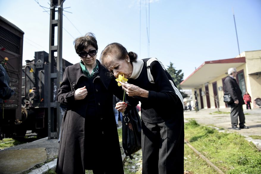 FILE - In this Sunday, March 15, 2015 file photo, Mina Beneroubi, a survivor of the Holocaust, right, places flowers on rails at the old train station in the northern Greek town of Thessaloniki on the 72nd anniversary of the roundup and deportation of its Jews to Nazi extermination camps during World War II. It was 1943 and the Nazis were deporting Greece’s Jews to Poland’s death camps. Hitler’s genocidal accountants reserved a chilling twist: The Jews had to pay their train fare. The total bill for 58,585 Jews sent to Auschwitz and other camps came to over 2 million Reichsmark - more than 25 million ($27 million) euros in today’s money. The Jewish community of Thessaloniki, Greece’s biggest, says it is examining the possibility of reclaiming the rail fares from Germany - and with seven decades of interest the amount would be enormous. (AP Photo/Giannis Papanikos,File)
