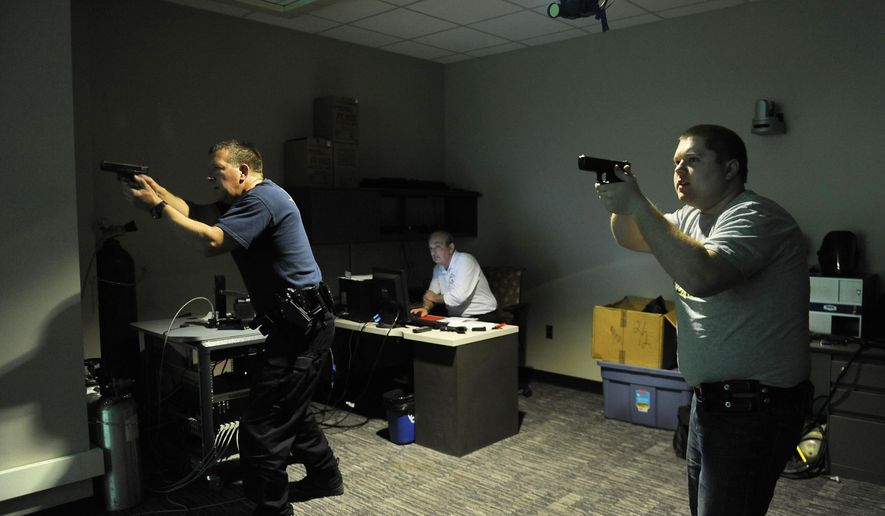 In a March 18, 2015 photo, Pat Schneider, left, and Kevin Ingrody, both officers with the Garden City Police Dept., train using a simulator that displays real life scenarios, in Livonia, Mich. Schoolcraft College course instructes police officers on simulators in a "Shoot-Don't shoot" scenario designed to train officers with help of MCOLES grants. The Michigan Commission on Law Enforcement Standards recently announced it won't accept competitive grant applications, which typically reflect 40 percent of funds provided for overall officer training, for next year. (AP Photo./The Detroit News, Clarence Tabb Jr.)
