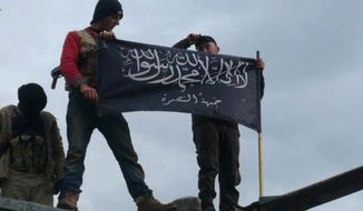 Rebels from al Qaeda-affiliated Jabhat al-Nusra, also known as the Nusra Front, wave their brigade flag as they step on the top of a Syrian air force helicopter at Taftanaz air base on Jan. 11, 2013. (Associated Press) **FILE**