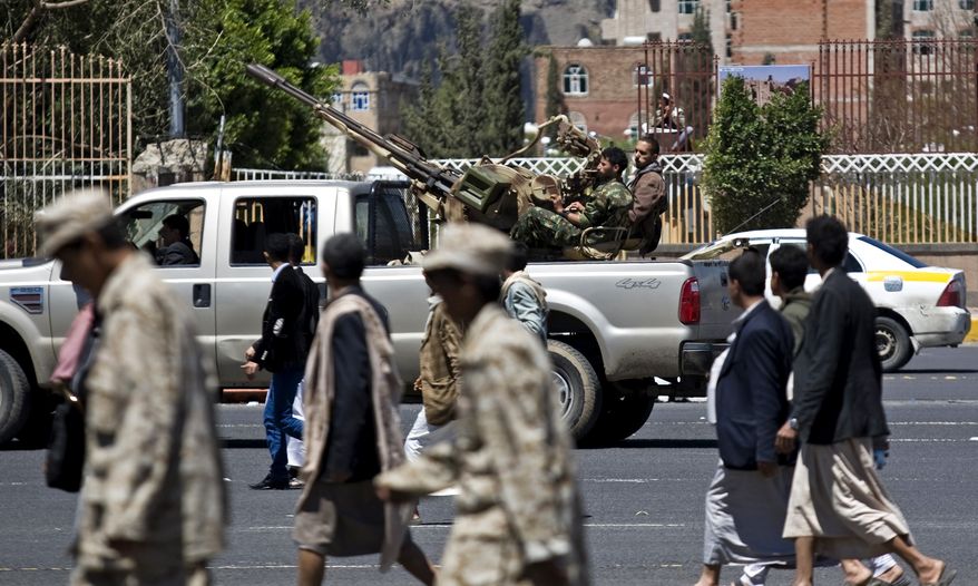 Houthi Shiite fighters (background) patrol as their comrades attend the funeral procession of victims who were killed from triple suicide bombings that hit a pair of mosques in Sanaa, Yemen, on Wednesday. (Associated Press)