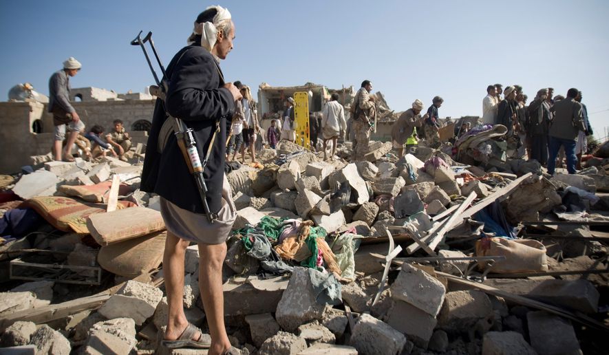 A Houthi Shiite fighter stands guard as people search for survivors under the rubble of houses destroyed by Saudi airstrikes near Sanaa airport in Yemen, Thursday. Saudi Arabia launched airstrikes targeting military installations in Yemen held by Shiite rebels. (Associated Press)