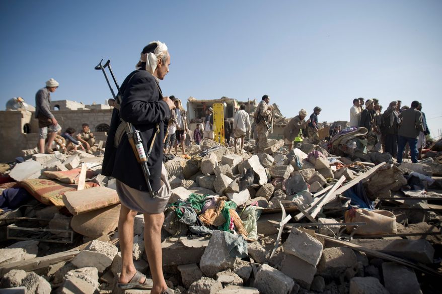 A Houthi Shiite fighter stands guard as people search for survivors under the rubble of houses destroyed by Saudi airstrikes near Sanaa airport in Yemen, Thursday. Saudi Arabia launched airstrikes targeting military installations in Yemen held by Shiite rebels. (Associated Press)