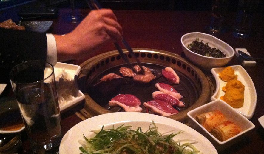 This Feb. 26, 2015 photo shows meat being cooked on a tableside Korean barbecue grill at Gaonnuri restaurant in New York. Gaonnuri is located on the 39th floor in the penthouse of a building on West 32nd Street, known as Korea Way. The district, also called Koreatown or K-town, is known for Korean restaurants and karaoke bars. (AP Photo/Beth J. Harpaz)