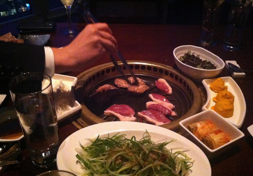 This Feb. 26, 2015 photo shows meat being cooked on a tableside Korean barbecue grill at Gaonnuri restaurant in New York. Gaonnuri is located on the 39th floor in the penthouse of a building on West 32nd Street, known as Korea Way. The district, also called Koreatown or K-town, is known for Korean restaurants and karaoke bars. (AP Photo/Beth J. Harpaz)