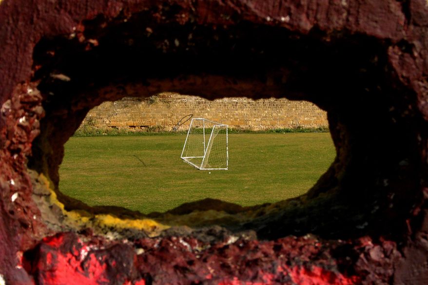 FILE - In this Wednesday, Nov. 6, 2013, file photo, a hole in a wall with a view of a soccer pitch inside the United Nations controlled buffer zone separating ethnically-split Cyprus in the capital Nicosia. Six decades of soccer separation on ethnically divided Cyprus may be at its end as breakaway Turkish Cypriots are poised to join the ranks of the Cyprus Football Association to bring the sport under a single administrative roof. Cyprus Turkish Football Association International Relations Co-ordniator Deniz Birinci said on Friday, March 27, 2015, that Association President Hasan Sertoglu will on Monday set in motion the process to induct the CTFA into the Cyprus FA. (AP Photo/Petros Karadjias, File)