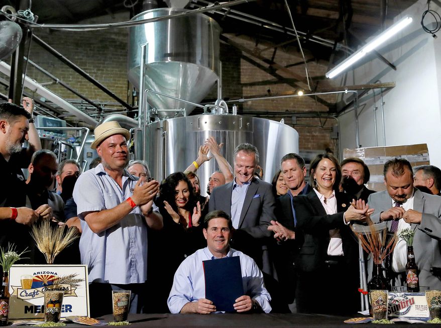 Supporters clap after Arizona Gov. Doug Ducey, center, signed Senate Bill 1030, Tuesday, March 31, 2015, at Four Peaks Brewery in Tempe, Ariz. The bill allows microbreweries to keep running their restaurants even as they grow into large beer producers. (AP Photo/Matt York)