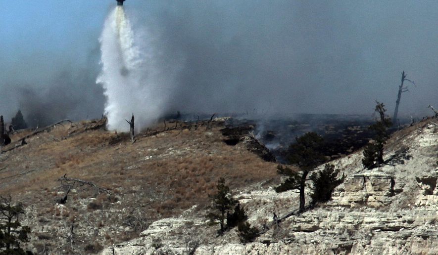 In this photo taken Monday, March 30, 2015, a South Dakota National Guard helicopter drops water on the Sheep Draw Fire near Camp Crook Road in Harding County, while working to contain the wildfire roughly 35 miles south of Buffalo, S.D. The Great Plains Fire Information office estimates that the Sheep Draw Fire has burned more than 10,000 acres since Saturday afternoon. The cause is still being investigated. (AP Photo/Rapid City Journal, Chris Huber) TV OUT