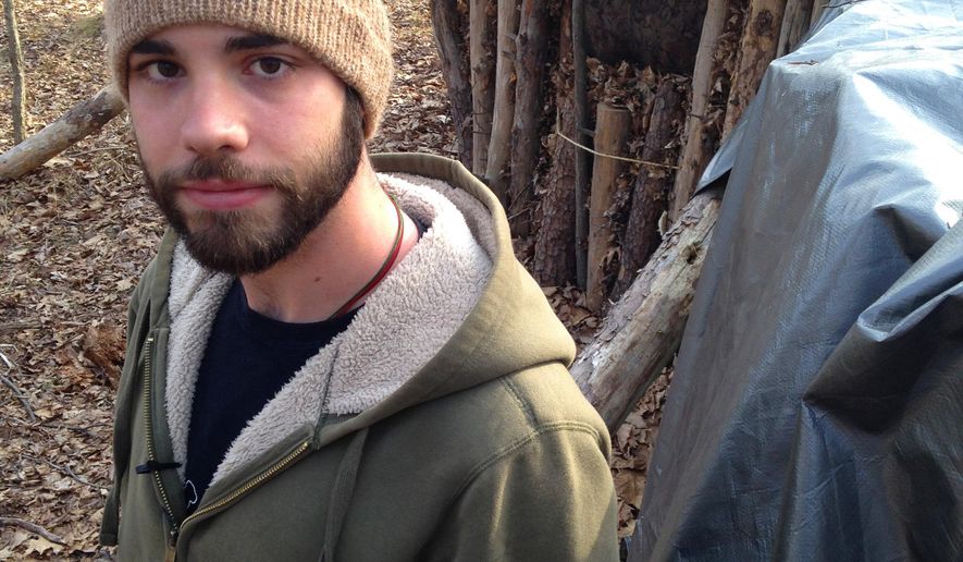 In this March 23, 2015 photo, Dylan Miller, a senior at Juniata College, poses in front of his shelter in the woods near campus in Huntingdon, Pa. For his senior research project on simple living, Miller decided to emulate Thoreau instead of just reading his work. So, deep in the woods about a half-hour's walk from campus, he built a hut out of fallen trees, leaves and a tarp - unheated, no plumbing - and has been living there since the beginning of the school year, studying by lantern and chasing away the occasional bear. (AP Photo/Michael Rubinkam)