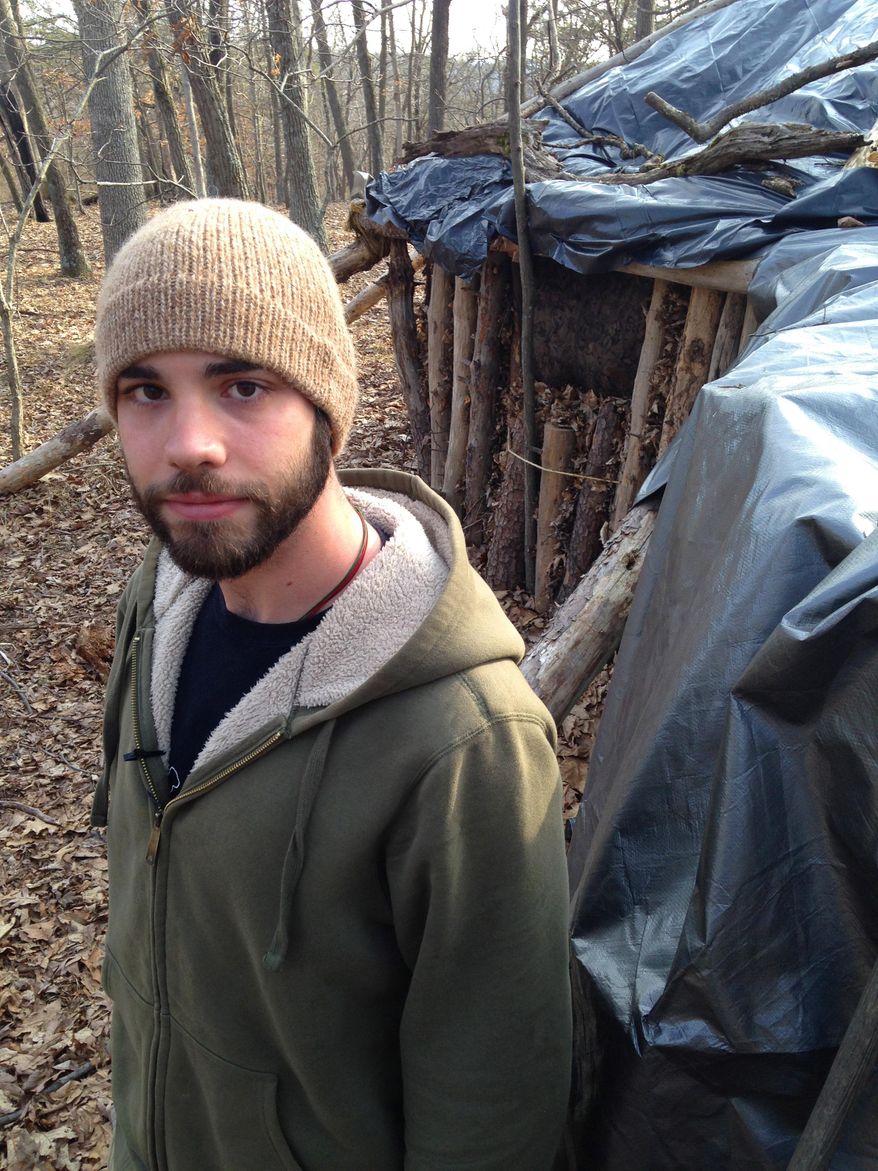 In this March 23, 2015 photo, Dylan Miller, a senior at Juniata College, poses in front of his shelter in the woods near campus in Huntingdon, Pa. For his senior research project on simple living, Miller decided to emulate Thoreau instead of just reading his work. So, deep in the woods about a half-hour's walk from campus, he built a hut out of fallen trees, leaves and a tarp - unheated, no plumbing - and has been living there since the beginning of the school year, studying by lantern and chasing away the occasional bear. (AP Photo/Michael Rubinkam)