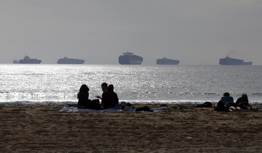 FILE - In this Feb. 20, 2015 file photo, people sit on the sand in Sunset Beach, Calif., as loaded cargo ships are anchored outside the Ports of Long Beach and Los Angeles. A tentative contract agreement that restored the flow of international trade through West Coast seaports earlier this year took a big step closer to becoming official, Friday, April 3, 2015 as representatives of the dockworkers' union overwhelmingly recommended that rank-and-file members vote to approve the deal. Difficult contract negotiations nearly closed 29 seaports from San Diego to Seattle, causing major delays in the delivery of billions of dollars of imports and exports. (AP Photo/Jae C. Hong, File)