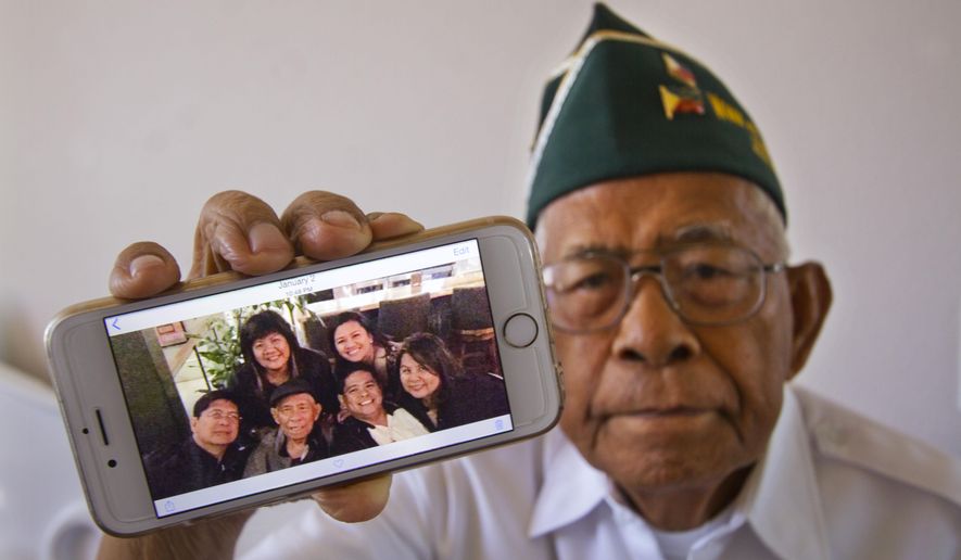 FOR RELEASE SUNDAY, APRIL 5, 2015, AT 2:00 A.M. HST.- In this March 27, 2015 photo, Filipino World War II veteran Artemio Caleda holds up a family photo at his home in Ewa Beach, Hawaii. Although the shrapnel scar Caleda picked up picked up during World War II is now seven decades old and faint, it serves as a stinging reminder that Caleda is still fighting a battle: to have his three grown sons join him in the United States. (AP Photo/Honolulu Star-Advertiser, Dennis Oda)