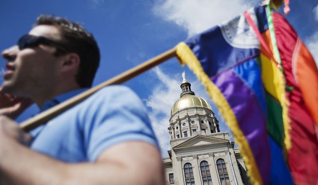 The dome of the Capitol stands in the background as Stephen Saras, of Atlanta, holds a rainbow colored flag during a rally against a contentious &quot;religious freedom&quot; bill, Tuesday, March 17, 2015, in Atlanta. The Georgia Senate gave decisive approval to the bill, one of a wave of measures surfacing in at least a dozen states that critics say could provide legal cover for discrimination against gays and transgender people. (AP Photo/David Goldman)
