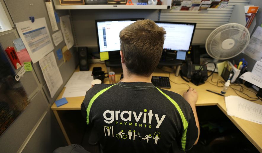 Austin Roos, a support team supervisor, works at his desk Wednesday, April 15, 2015, at Gravity Payments, a credit card payment processor based in Seattle. Gravity CEO Dan Price told his employees this week that he was cutting his roughly $1 million salary and using company profits so they would each earn a base salary of $70,000, to be phased in over three years. (AP Photo/Ted S. Warren)