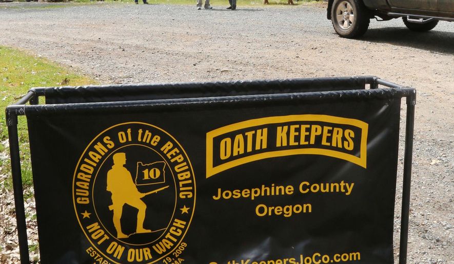 In this photo taken Tuesday, April 14, 2015, an Oath Keepers, constitutional activists, sign marks the entrance to a property on Camp Joy Road near Merlin, Ore, while armed Oath Keepers security guards hover in the background. (Timothy Bullard/The Daily Courier via AP)  **FILE**