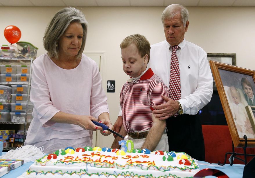In this photo taken Tuesday, April 14, 2015, Sandra Pike lights a number 30 candle as her husband, Jerry, right, stands beside their son Joey as guests wait to sing "Happy Birthday" to Joey for his birthday celebration at Eagles' Wings in Coker, Ala. When 6-month-old Joey Pike was diagnosed with Marshall-Smith syndrome, a rare intellectual and physical disability, doctors said he probably wouldn't live past 3. Joey defied the odds. Family, friends and others celebrated his 30th birthday Tuesday with a party. (Erin Nelson /The Tuscaloosa News via AP) MANDATORY CREDIT, NO SALES