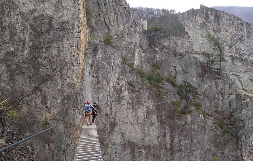 In this March 24, 2015 photo, Matt Karlson, right, supervisor for the NROCKS Outdoor Center and Chris Ward, operations manager for the center, walk across a suspension bridge that stretches 200 feet between rock formations at 150 feet above ground in Circleville, W. Va. A recent study commissioned by the Appalachian Regional Commission cites West Virginia's Nelson Rocks and Seneca Rocks, a formation to the north owned by the National Park Service, as keys to Pendleton County's “tremendous potential as a tourism destination.” But like all tourism in the Mountain State, it faces challenges. (AP Photo/ Jonathan Drew)