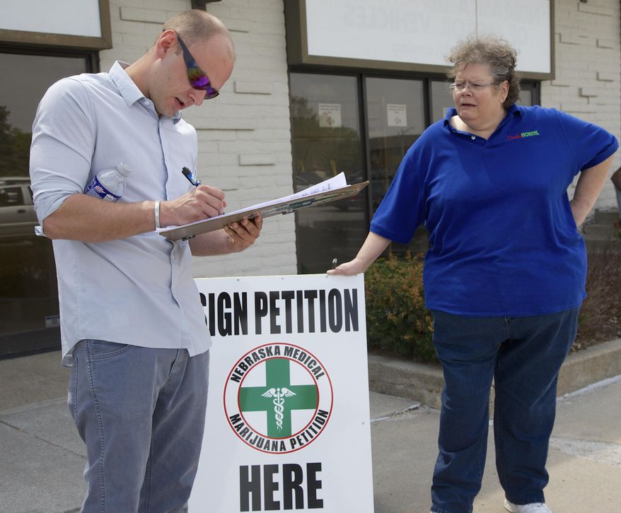 Activist Maggie Graham, right, collects a signature from Nick Wages, of Omaha, for a petition to place medical marijuana on the ballot in Omaha, Neb., Friday, April 17, 2015. A new Nebraska law that lifts restrictions on petition circulators may have given a boost to an unlikely group: advocates for medical marijuana. Frustrated by inaction in the Nebraska Legislature, supporters say they're circulating signatures to place the issue before voters in 2016 _ and the petition law just made their job easier. (AP Photo/Nati Harnik)