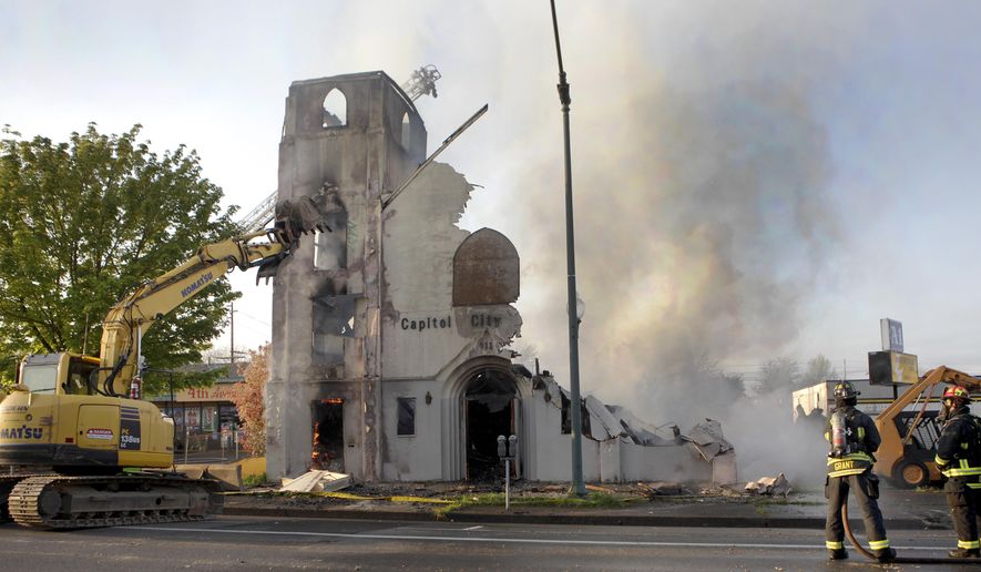 A large excavator begins the demolition of the fire damaged Capitol City Studios after an early morning fire gutted the vacant building in Olympia, Wash., on Monday, April 20, 2015. Firefighters rescued a woman from the former church after flames drove her to the roof. The building had been empty for years. Most recently it was Capitol City Studios. It originally was the Foursquare Gospel church of Olympia. A man who also was on the roof jumped off, hurting his ankle, and ran away. (Steve Bloom/The Olympian via AP)
