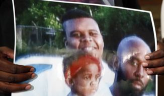 Michael Brown Sr., holds up a photo of himself, at right, his son, Michael Brown, top left, and a young child during a news conference Monday, Aug. 11, 2014, in Jennings, Mo. Michael Brown, 18, was shot and killed in a confrontation with police in the St. Louis suburb of Ferguson, Mo, on Saturday, Aug. 9, 2014.(AP Photo/Jeff Roberson)