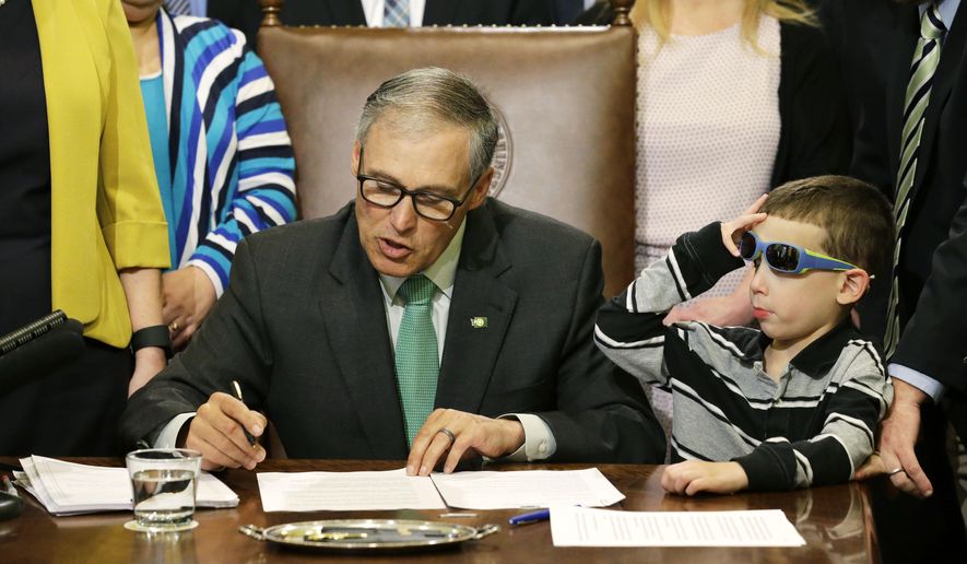 Haiden Day, 6, right, who has Dravet Syndrome, a form of epilepsy that his parents treat with medical marijuana, looks on as Washington Gov. Jay Inslee, left, signs a bill Friday, April 24, 2015 at the Capitol in Olympia, Wash., that overhauls Washington's medical marijuana market. The bill also creates a voluntary database of patients and cracks down on unregulated dispensary sales. Inslee has said the measure is needed now that the state's voter-approved recreational market is in place. (AP Photo/Ted S. Warren)