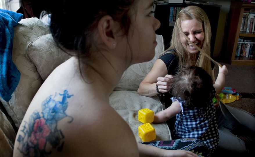 ADVANCE FOR USE SATURDAY, APRIL 25, 2015, AND THEREAFTER- In this April 20, 2015 photo, Cory Campbell, left, looks on as her daughter 8-month-old Arya Lewis, plays with nurse Jenni Hughes, at their home in Rathdrum, Idaho. Panhandle Health District offers a program that teams nurses up with low-income moms for the first two years of the child's life. ((Kathy Plonka/The Spokesman-Review via AP) COEUR D'ALENE PRESS OUT