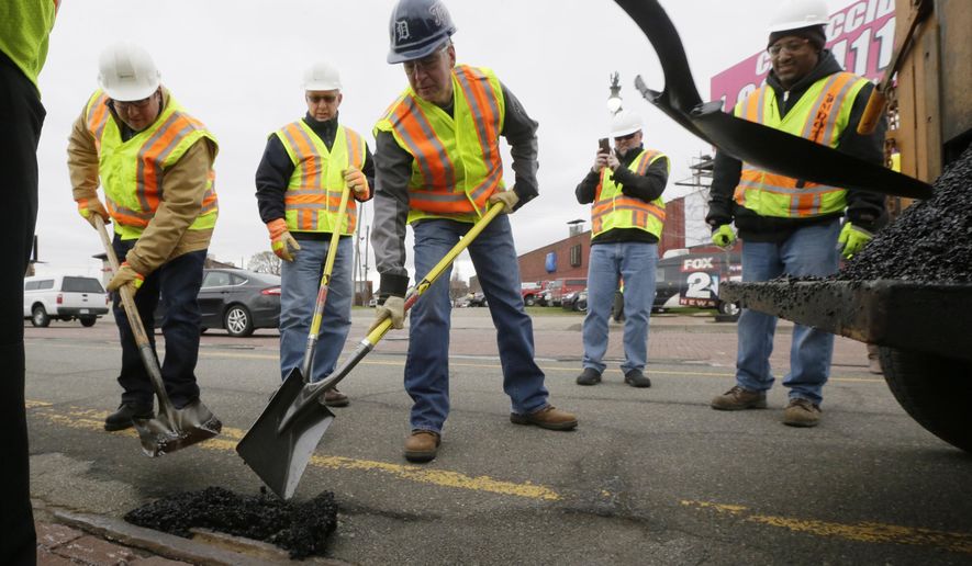 In this Thursday, April 23, 2015 photo, Michigan Gov. Rick Snyder, center, helps patch a pothole on Michigan Ave., in Detroit. Michigan voters will decide the fate of a sales tax increase linked to road improvements because that’s what lawmakers proposed after deadlocking on directly raising taxes themselves. But in the months since, legislators have mostly kept quiet on what Gov. Snyder says is the most pressing issue facing the state. Few, in fact, replied to an Associated Press survey asking how they intend to vote on May 5. (AP Photo/Carlos Osorio)