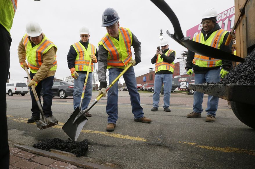 In this Thursday, April 23, 2015 photo, Michigan Gov. Rick Snyder, center, helps patch a pothole on Michigan Ave., in Detroit. Michigan voters will decide the fate of a sales tax increase linked to road improvements because that’s what lawmakers proposed after deadlocking on directly raising taxes themselves. But in the months since, legislators have mostly kept quiet on what Gov. Snyder says is the most pressing issue facing the state. Few, in fact, replied to an Associated Press survey asking how they intend to vote on May 5. (AP Photo/Carlos Osorio)