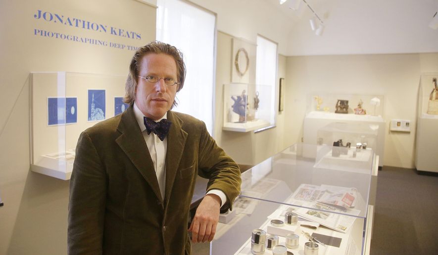 Jonathon Keats poses in his "millennium camera" exhibit at the Mead Art Museum on the Amherst College campus Thursday, April 16, 2015, in Amherst, Mass. Keats, a San Francisco-based writer who describes himself as an experimental philosopher and conceptual artist, has designed a camera he plans to perch atop a church-less steeple on the Amherst College campus, hoping the device will chronicle climate change by making a 1,000-year-long photograph of the Holyoke Range in western Massachusetts. (AP Photo/Stephan Savoia)