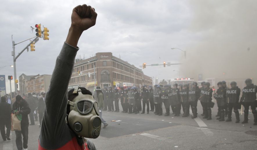 A demonstrator raises his fist as police stand in formation as a store burns, Monday, April 27, 2015, during unrest following the funeral of Freddie Gray in Baltimore. Gray died from spinal injuries about a week after he was arrested and transported in a Baltimore Police Department van. (AP Photo/Patrick Semansky)