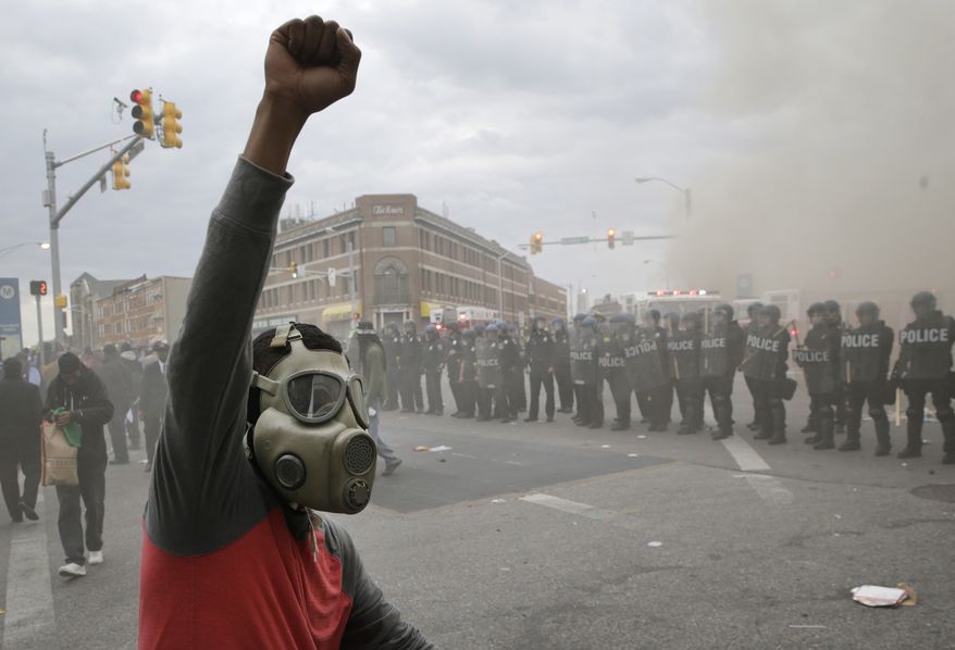 A demonstrator raises his fist as police stand in formation as a store burns, Monday, April 27, 2015, during unrest following the funeral of Freddie Gray in Baltimore. Gray died from spinal injuries about a week after he was arrested and transported in a Baltimore Police Department van. (AP Photo/Patrick Semansky)