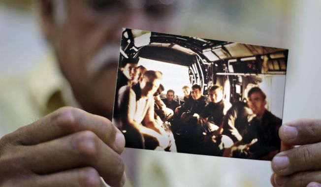 In this Tuesday, April 28, 2015 photo, former U.S. Marines Master Gunnery Sgt. Juan Valdez of Oceanside, California, holds a photo of himself, rear center, sitting on the last helicopter leaving the U.S. Embassy in Saigon on April 30, 1975, in Ho Chi Minh City, Vietnam. On the 40th anniversary of the fall of Saigon, 13 Marines  returned to dedicate a plaque to their two fallen brothers at the site of the old embassy, which is now the U.S. Consulate. (AP Photo/Dita Alangkara)