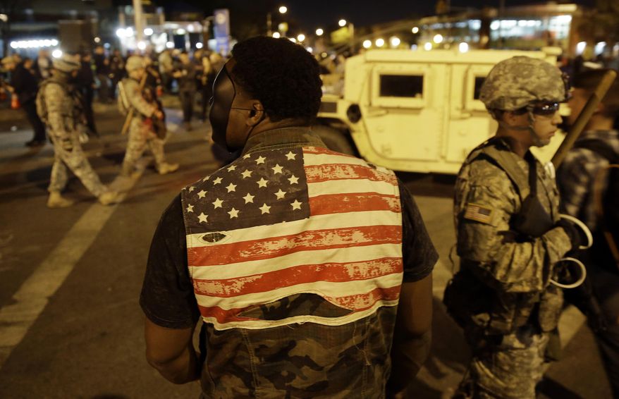 A protester watches soldiers pass as curfew approaches, Friday, May 1, 2015, in Baltimore. (AP Photo/Patrick Semansky)