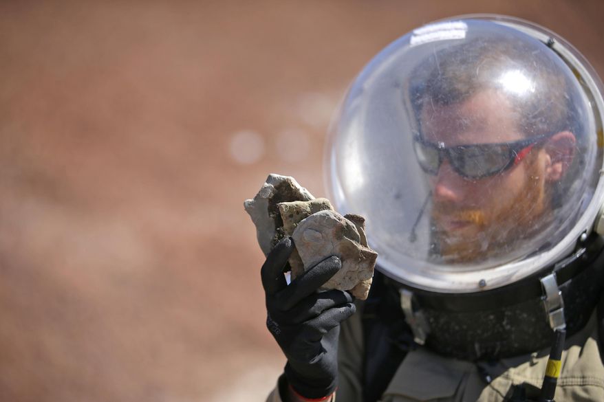 In this photo taken on Saturday, April 18, 2015, Florian Commans, crew biologist and greenhab officier, of Crew 153, studies a collection of rocks near the Mars Desert Research Station, in Hanksville, Utah. This isn’t Mars, but it’s resemblance to the red planet has made it a hot spot for teams of geologists, biologists and engineers from around the world who have been coming for more than a decade to simulate missions to the mysterious planet in hopes of providing critical research to for future trips to Mars. (AP Photo/Rick Bowmer)
