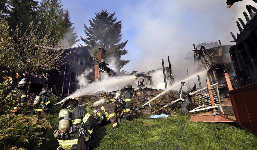Firefighters pour water on a home Thursday, April 30, 2015, in Seattle. The dramatic fire burned three houses in the West Seattle neighborhood, sending up plumes of black smoke visible for miles. (AP Photo/Elaine Thompson)