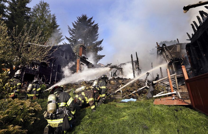 Firefighters pour water on a home Thursday, April 30, 2015, in Seattle. The dramatic fire burned three houses in the West Seattle neighborhood, sending up plumes of black smoke visible for miles. (AP Photo/Elaine Thompson)