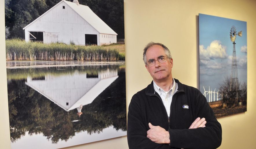 In this March 26, 2015 photo, photographer Ken Urban of Davenport, Iowa, poses with some of his photographs on display in the new addition of UnityPoint Health-Trinity in Rock Island, Ill. Artwork from 20 area artists is aimed to promote peace, comfort and recovery at the hospital. (Gary Krambeck/The Dispatch via AP)